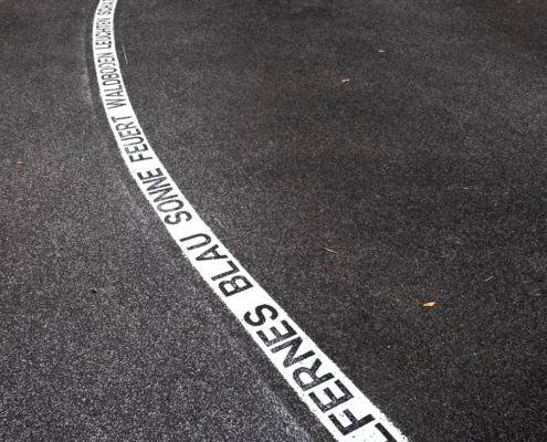Sicht auf auf einen asphaltierten Weg mit einer weißen Mittelmarkierung mit Text in schwarzer Farbe. Teil des 400 Meter langen Kunstprojekts "Himmelfernes" von craus-hahn beim CityLeaks Festival 2019 in Köln.
