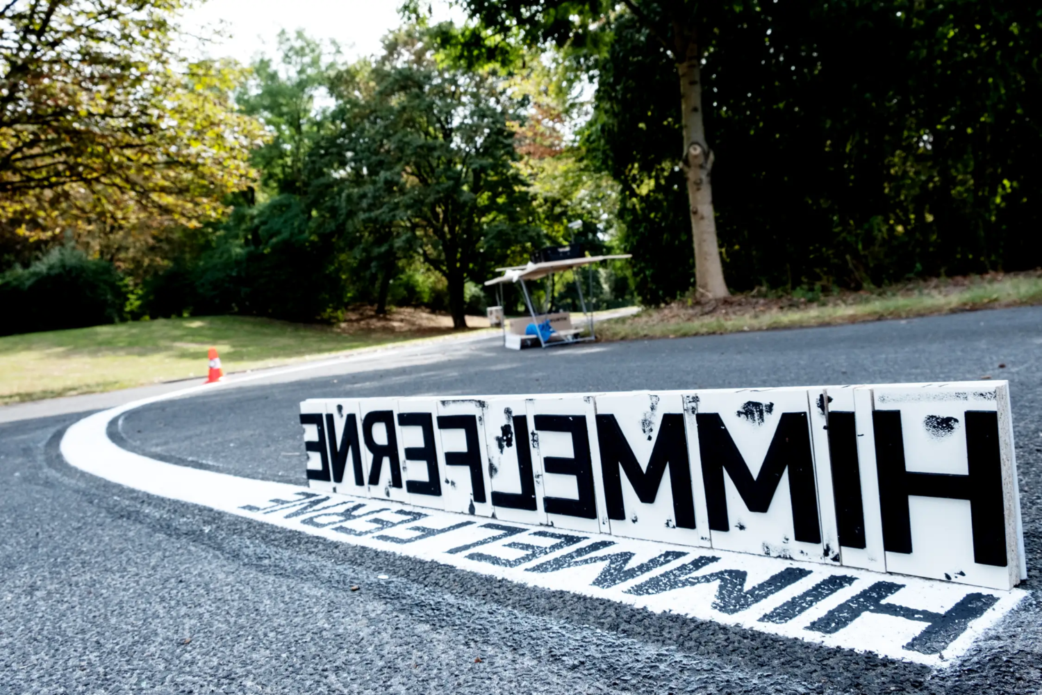 Himmelfernes, CityLeaks 2019hn9 Detail: asphaltierter Weg mit einer weißen Mittelmarkierung mit Textstempel (Ausschnitt) in schwarzer Farbe an gedrucktem Text "HIMMELFERNE". Teil des 400 Meter langen Kunstprojekts "Himmelfernes" von craus-hahn beim CityLeaks Festival 2019 in Köln.